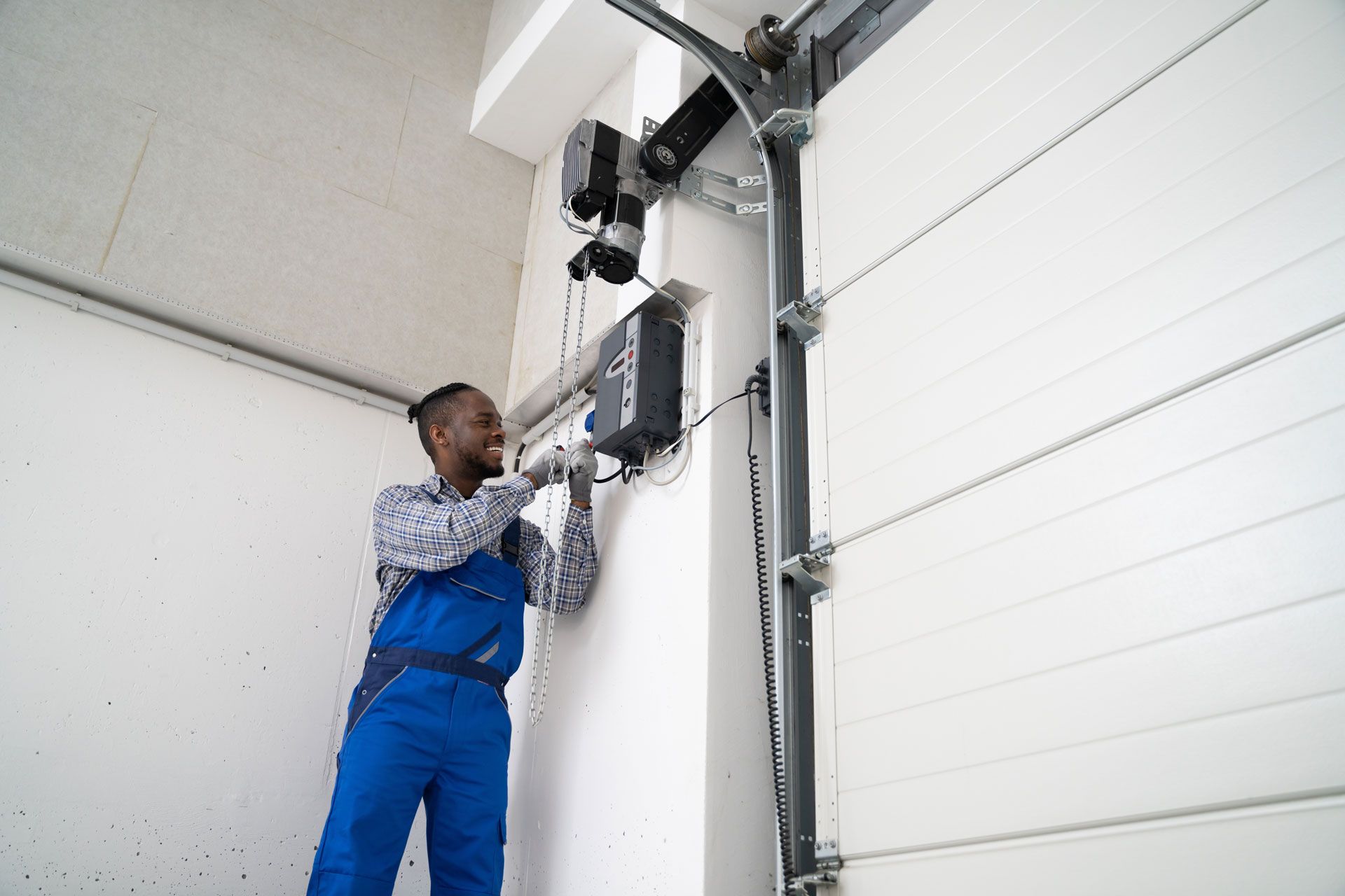 Technician in blue overalls adjusting a garage door opener on a white overhead door