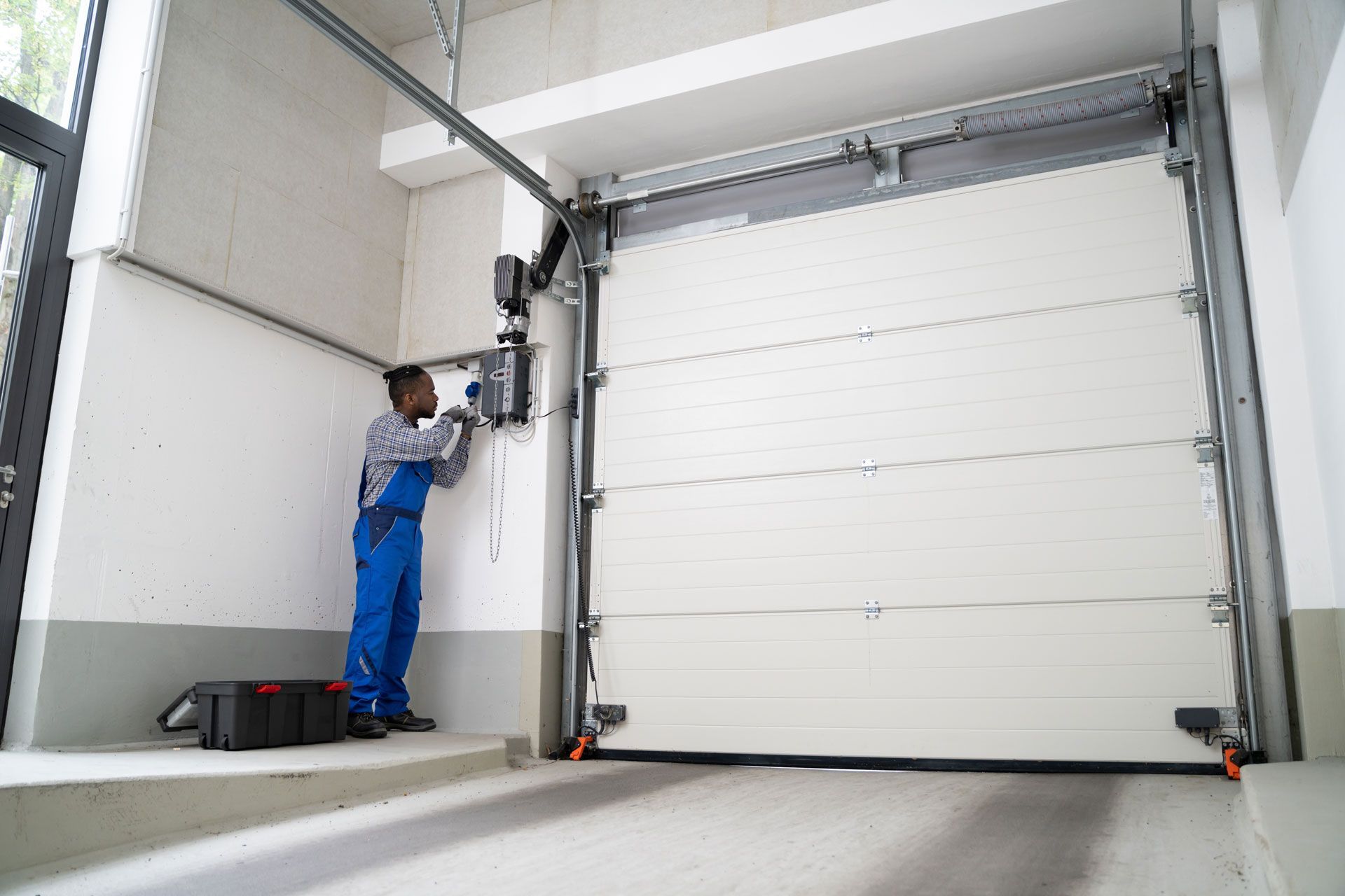 Worker adjusting a garage door opener on a large white industrial roll-up door