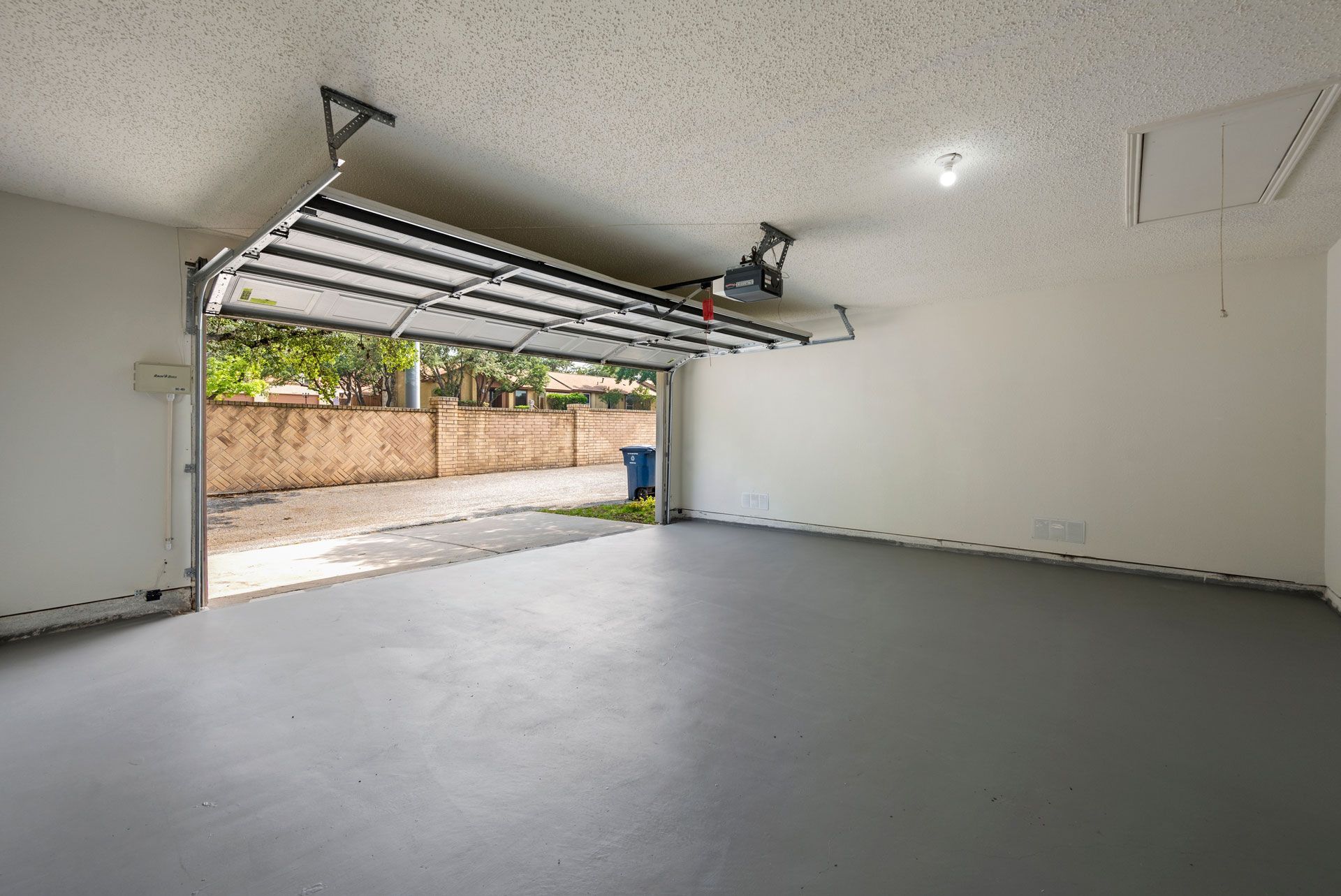 Empty two-car garage with open door, gray floor, white walls, and driveway view outside