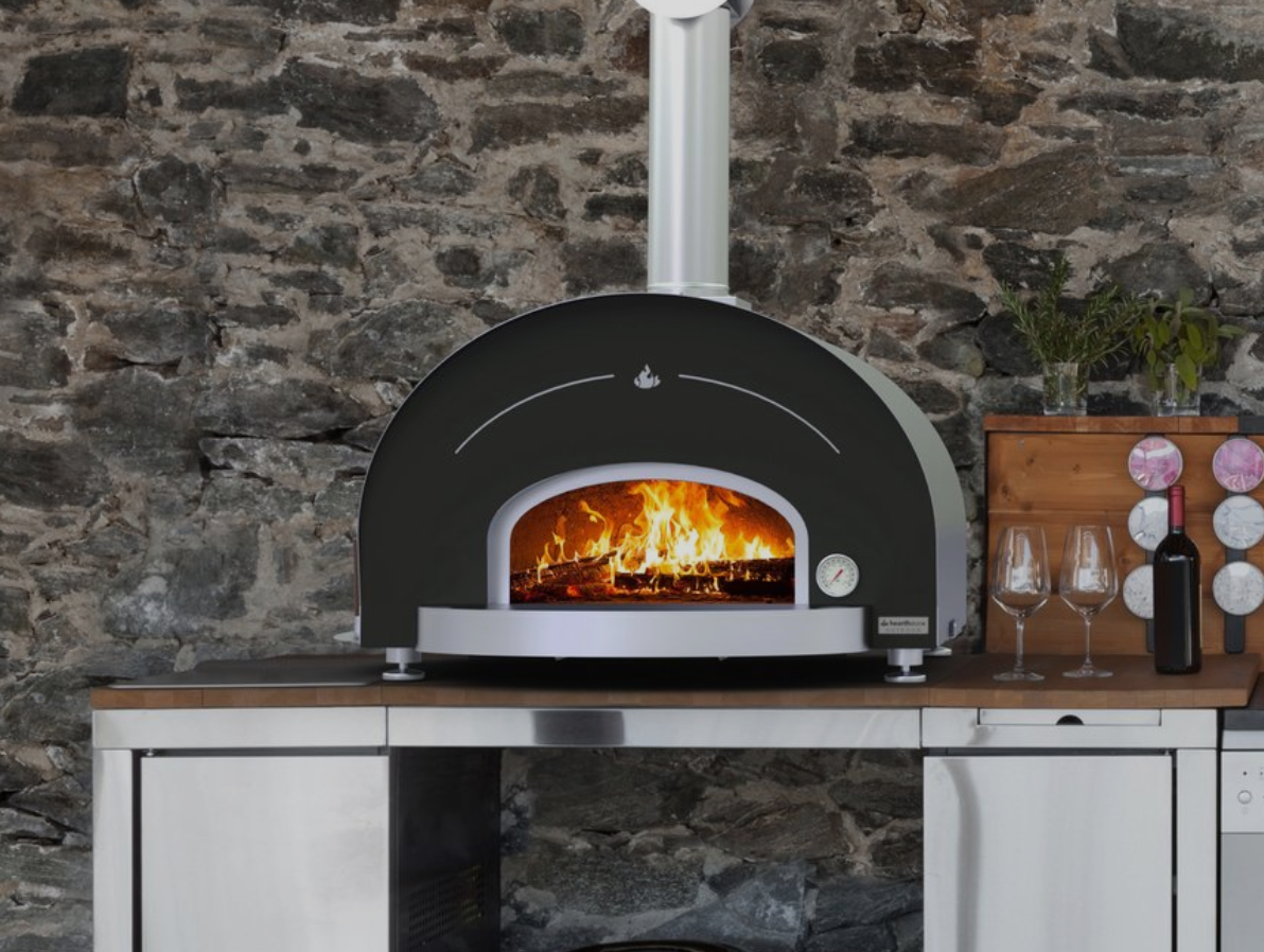 A pizza oven is sitting on a counter in front of a stone wall