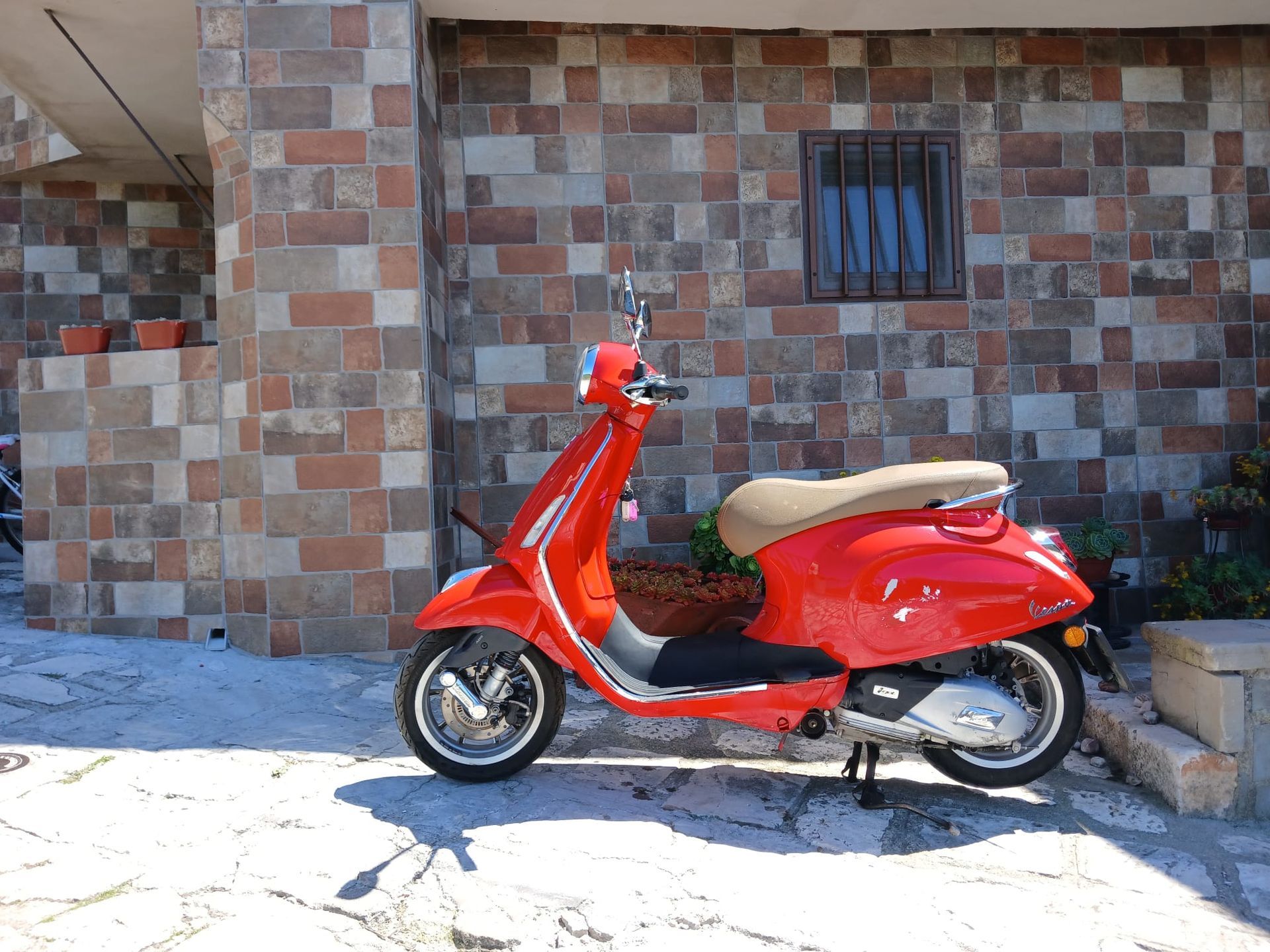 Red scooter parked beside a tiled wall in bright sunlight.
