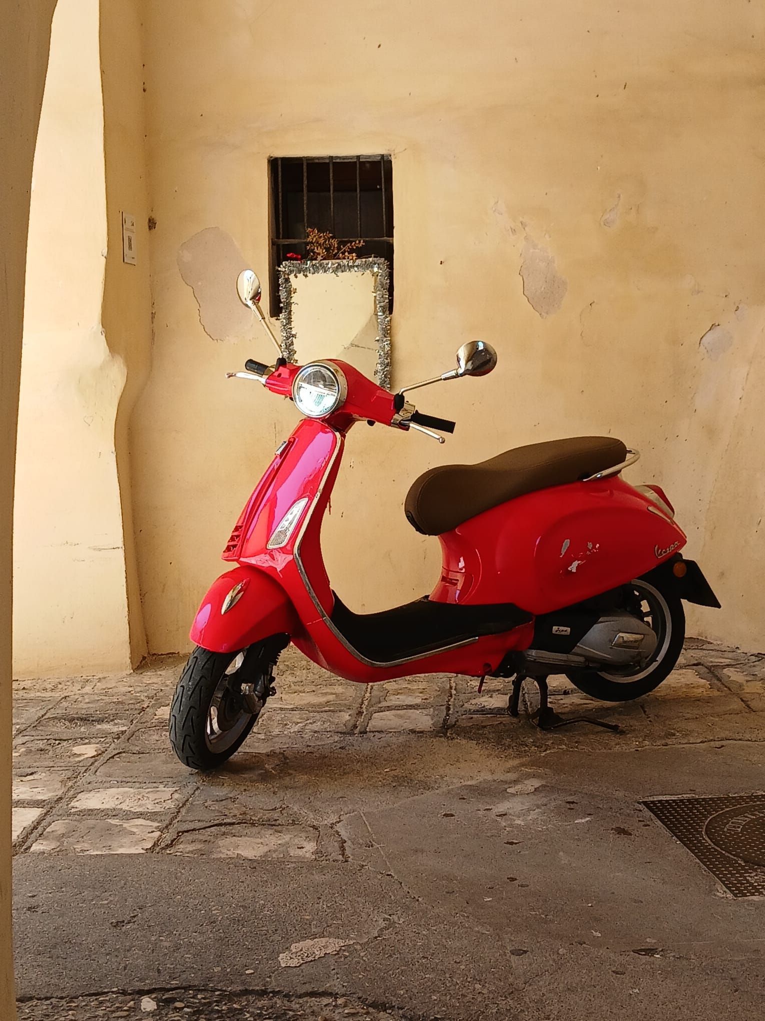 Red scooter parked in a beige indoor alcove with a cracked wall and concrete floor.