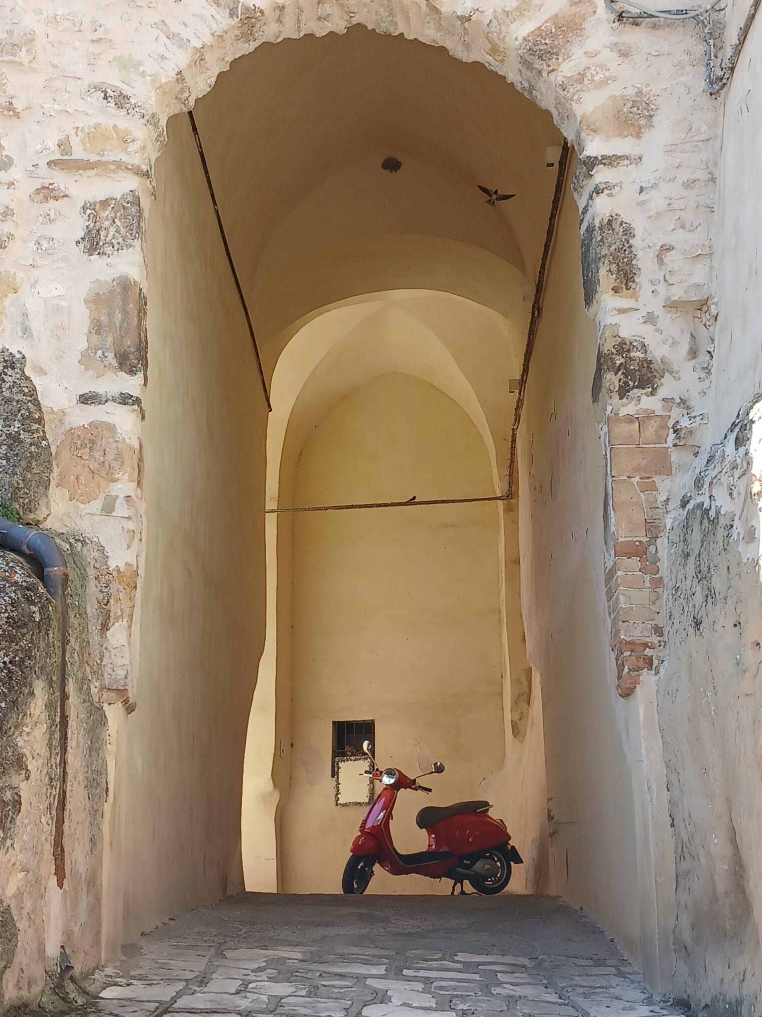 Narrow stone archway with a red scooter parked at the end of a dim corridor