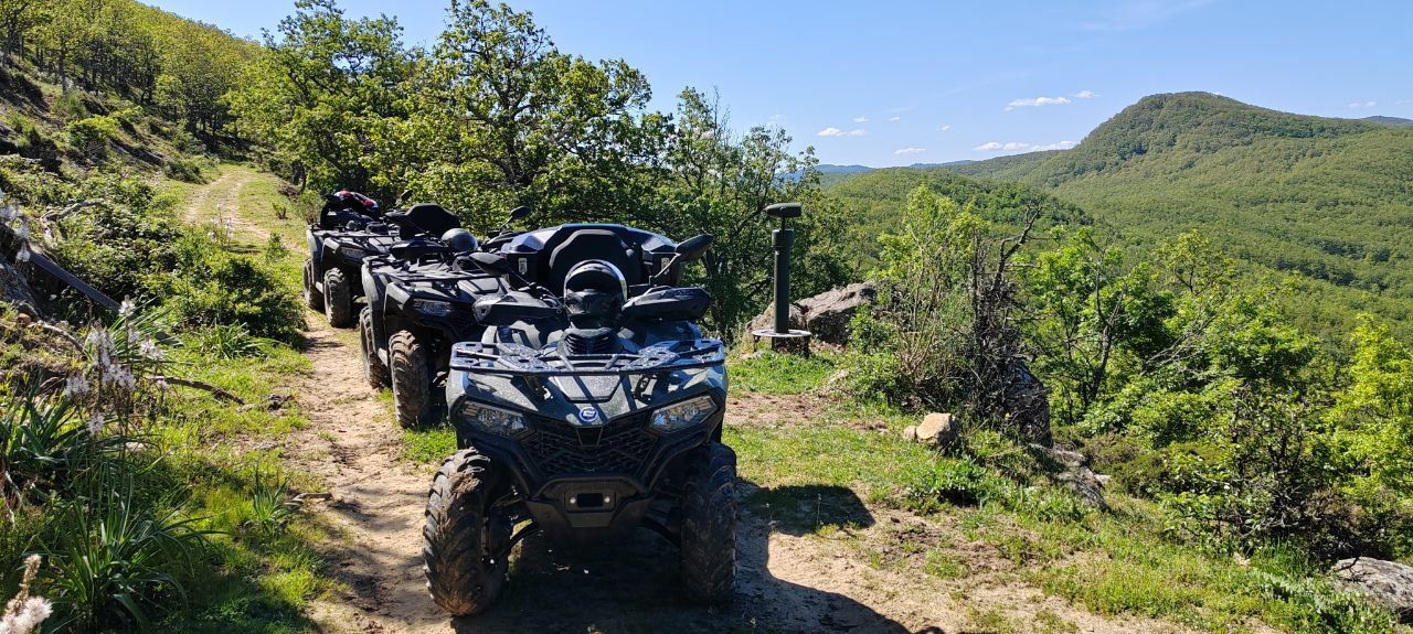 ATVs on a dirt trail in lush green hills under a bright blue sky