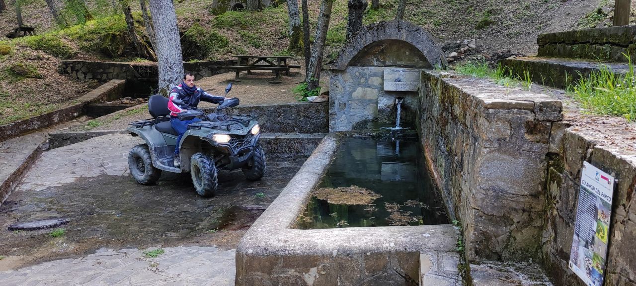 Person riding an ATV through a stone-lined water channel in a wooded park