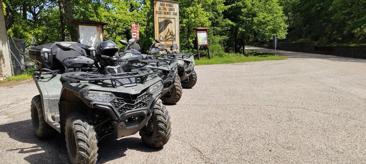 Three black ATVs parked on a gravel path in a wooded area
