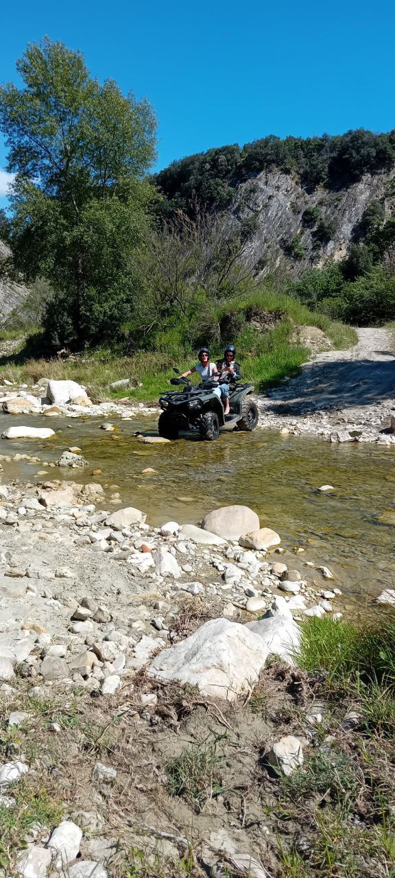 ATV crossing a shallow rocky stream in a sunny rural valley