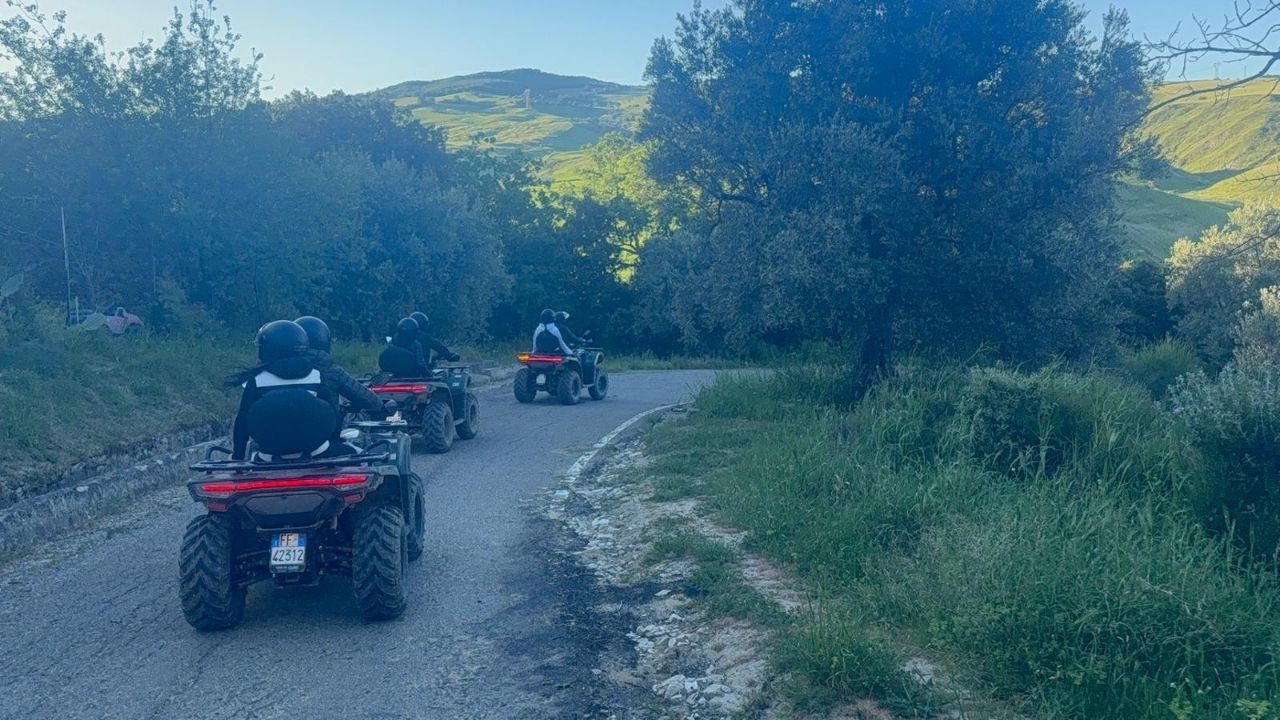 Three people riding ATVs on a gravel trail through a green, hilly countryside