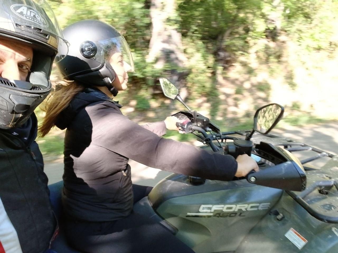Two people on a green ATV riding through a wooded trail