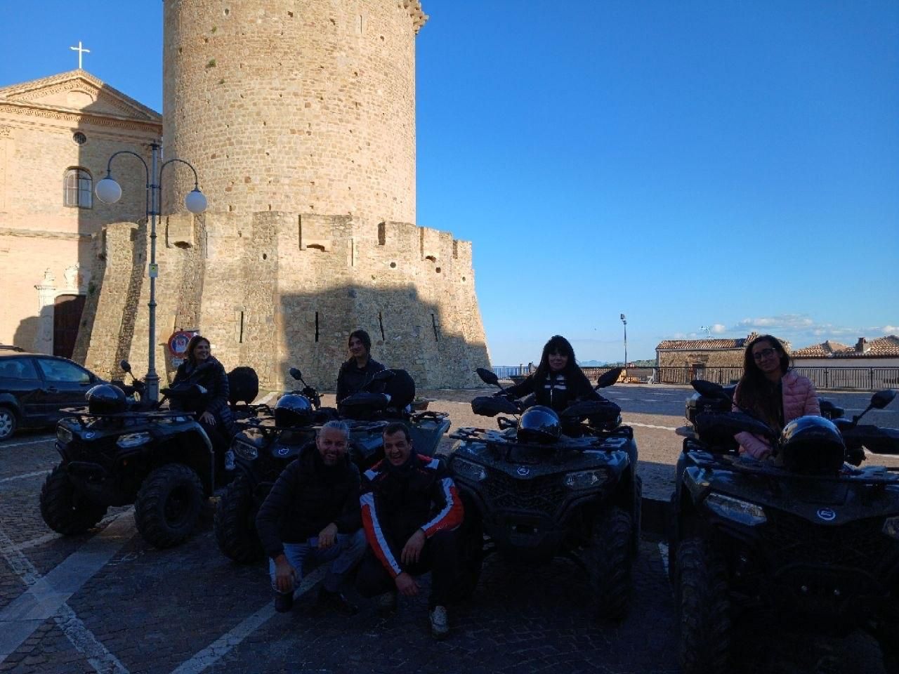 ATV riders posing in front of a stone castle tower on a sunny day