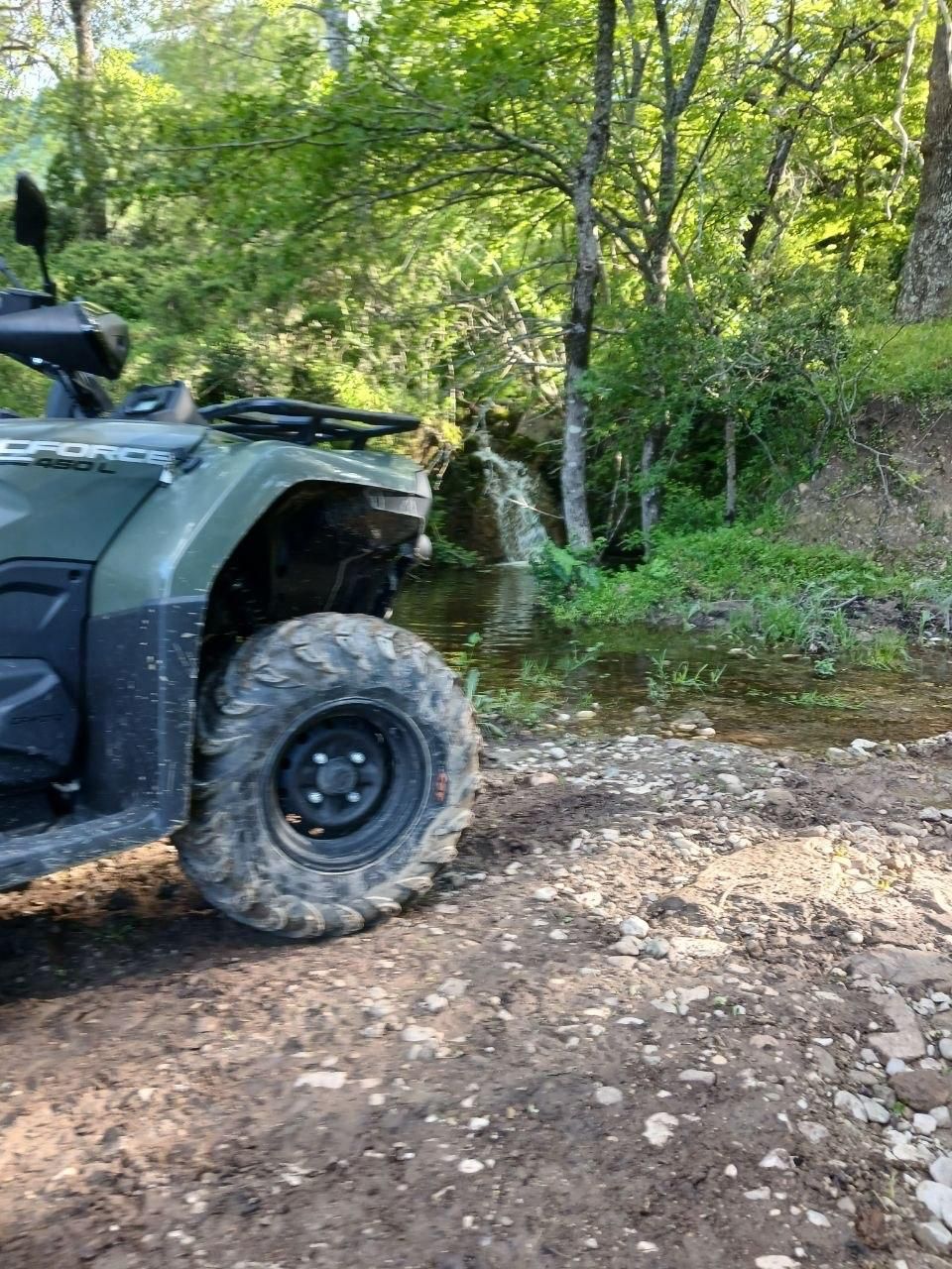 Off-road ATV parked on a muddy forest trail beside a wooded stream