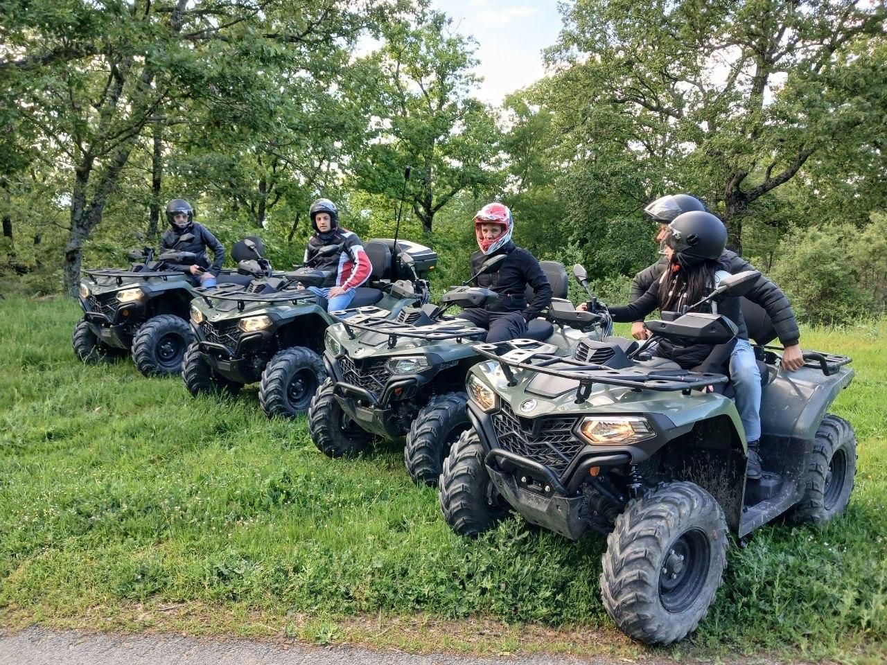 Four people on ATVs lined up on a grassy trail in a wooded area