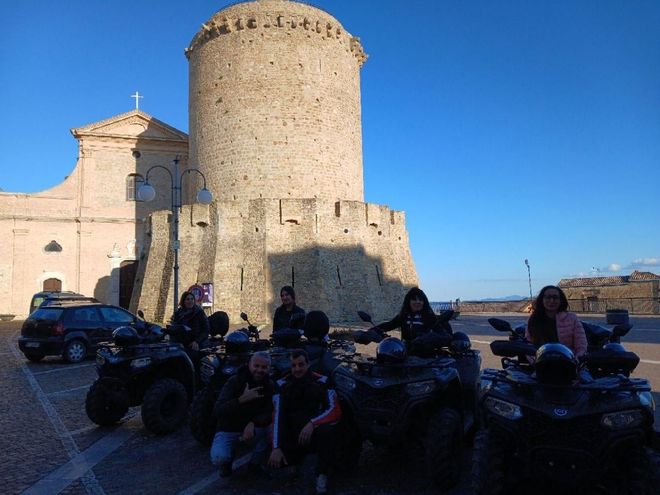 Quad parcheggiati in un cortile soleggiato accanto a una torre di pietra e a un edificio storico.
