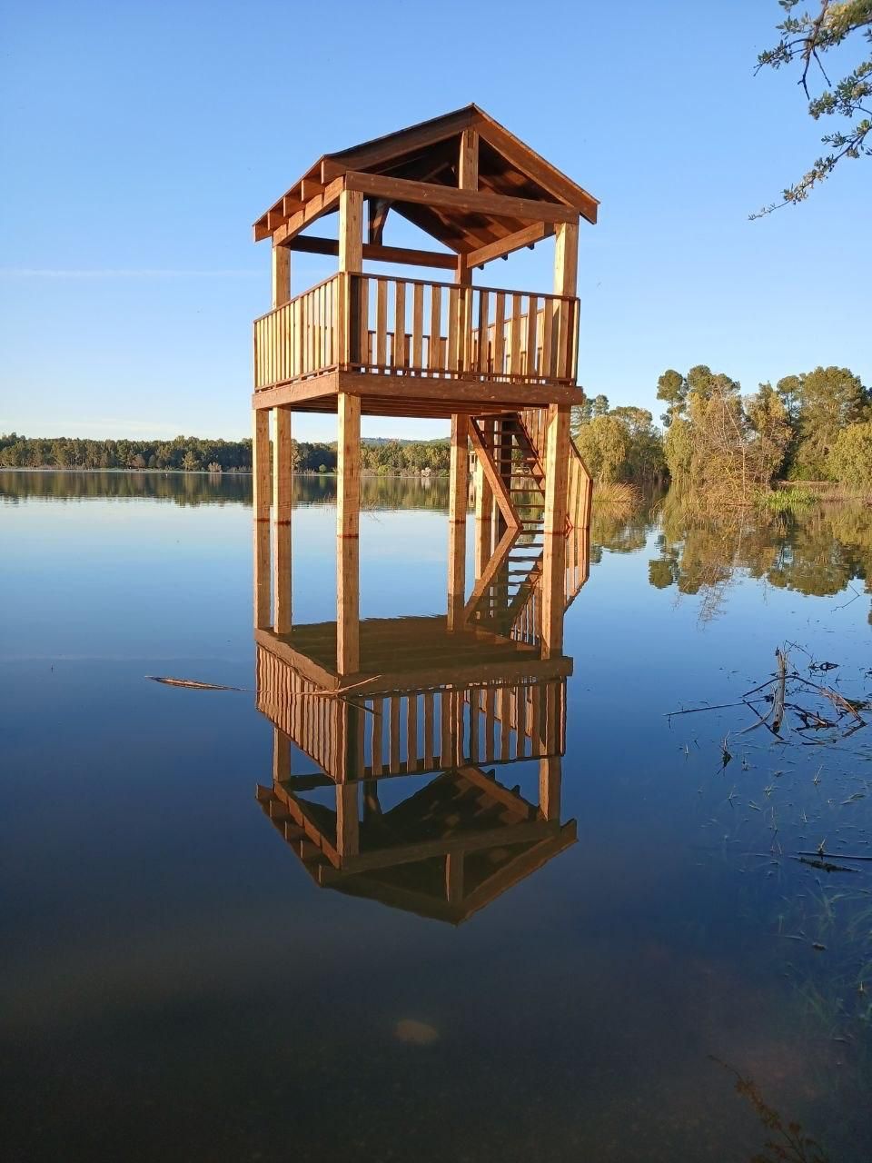 Wooden lakeside lookout tower reflected in calm water at sunset