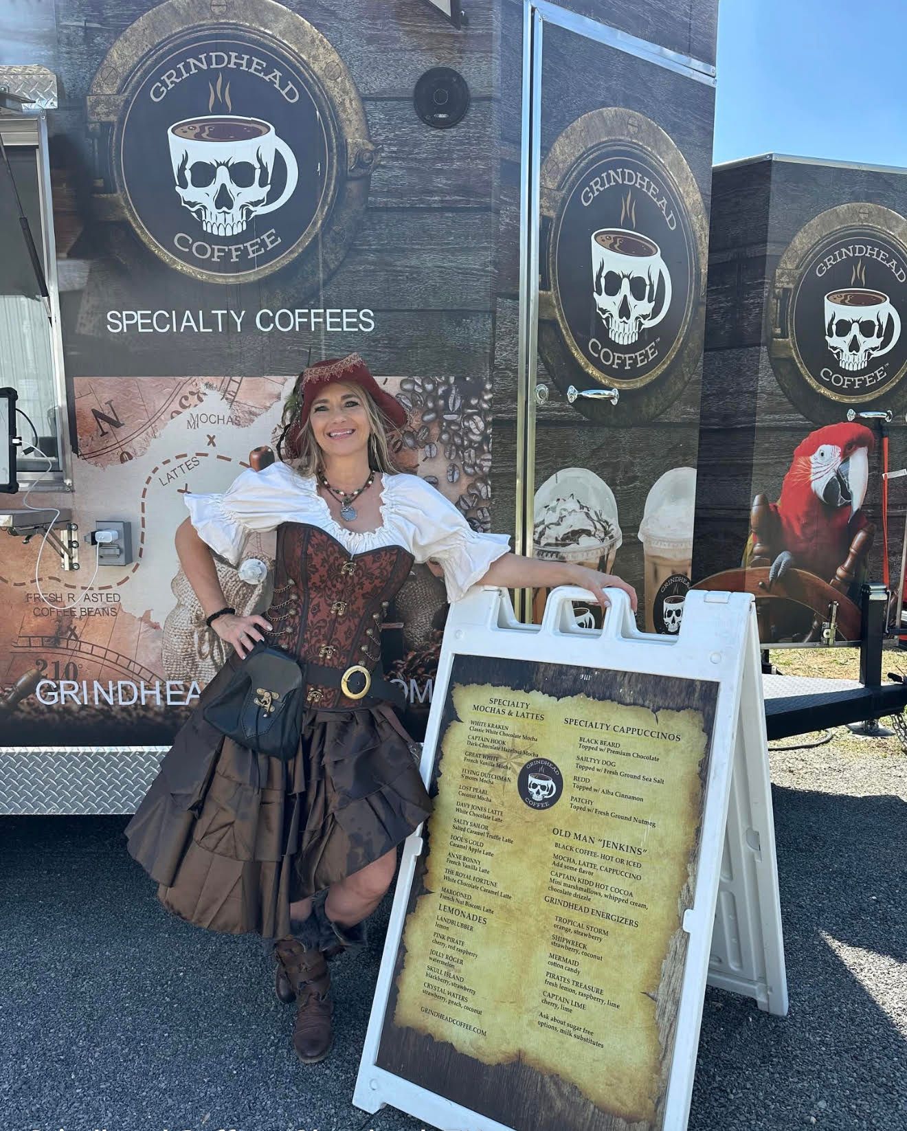 Woman behind a coffee shop counter holding iced coffees; wooden display with coffee bags.