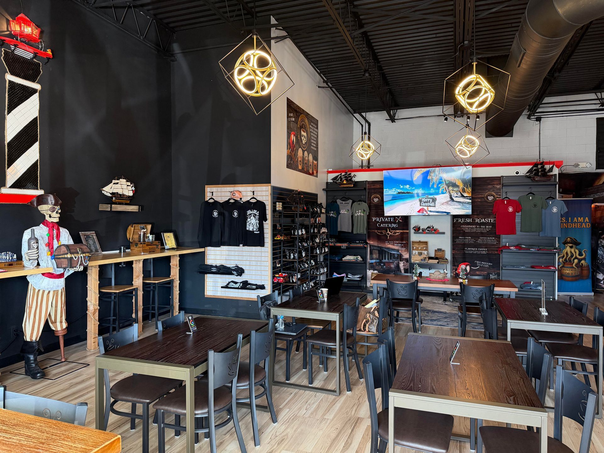 Interior of a shop with tables and chairs, displays of merchandise, and a TV screen.