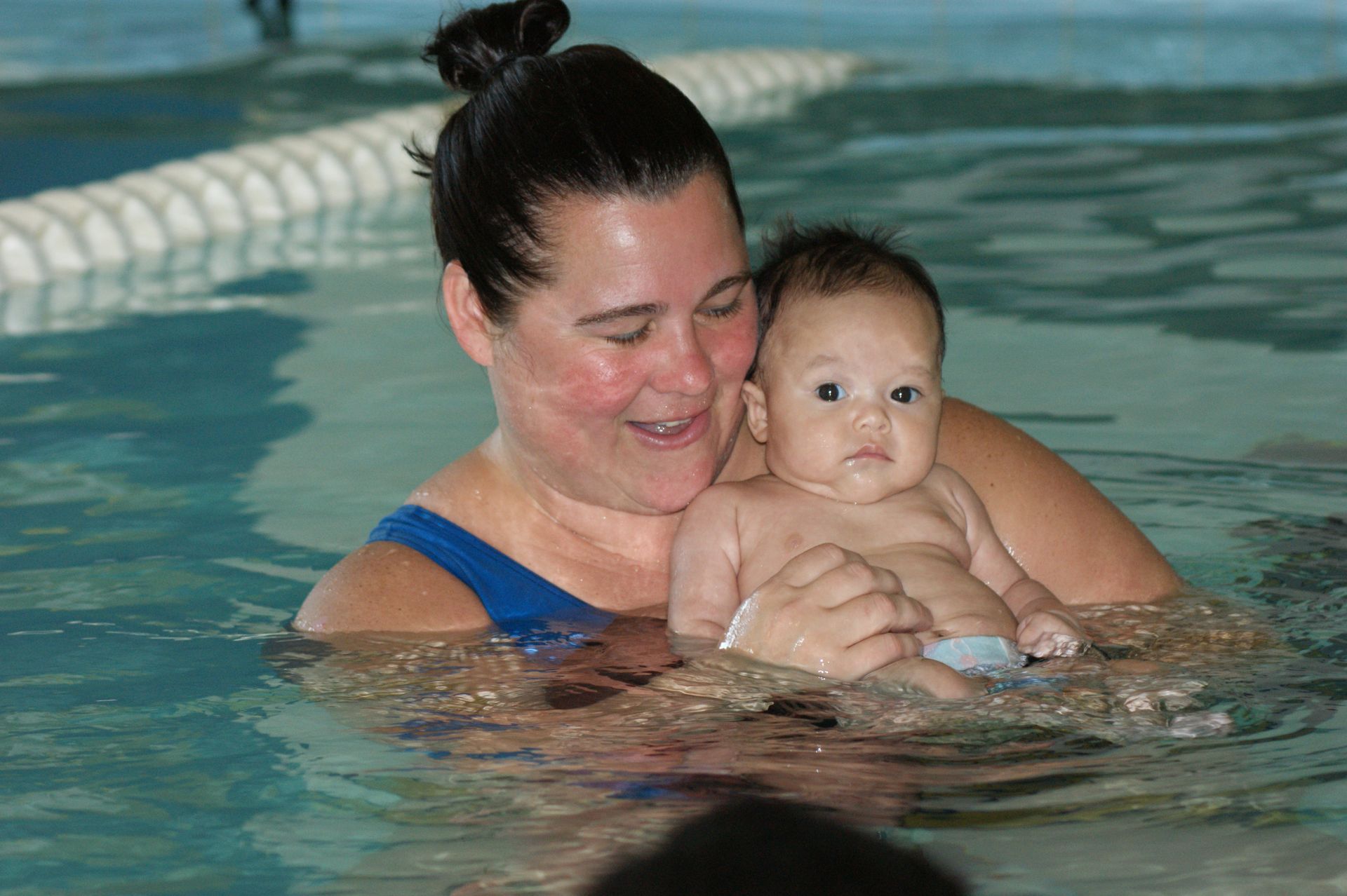 A woman is holding a baby in a swimming pool.