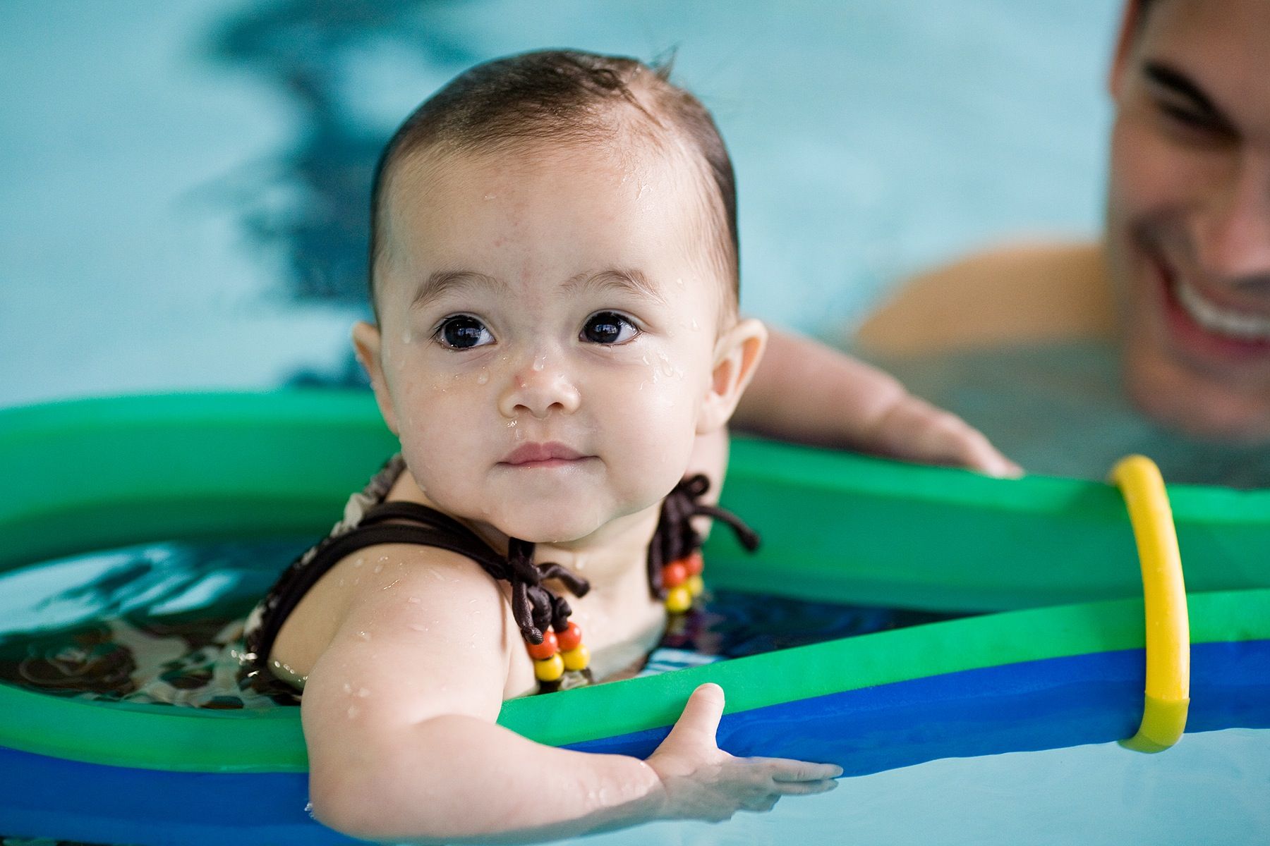 A baby is swimming in a pool with a man.