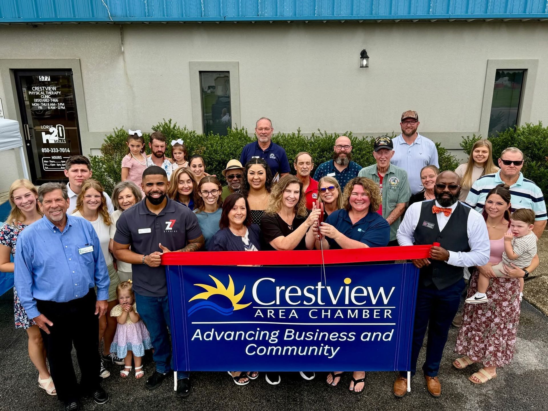 People gather for a Crestview Area Chamber ribbon-cutting ceremony, holding a banner.