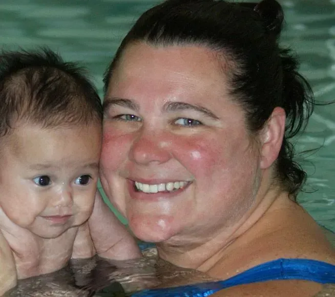 A woman is holding a baby in a pool and smiling