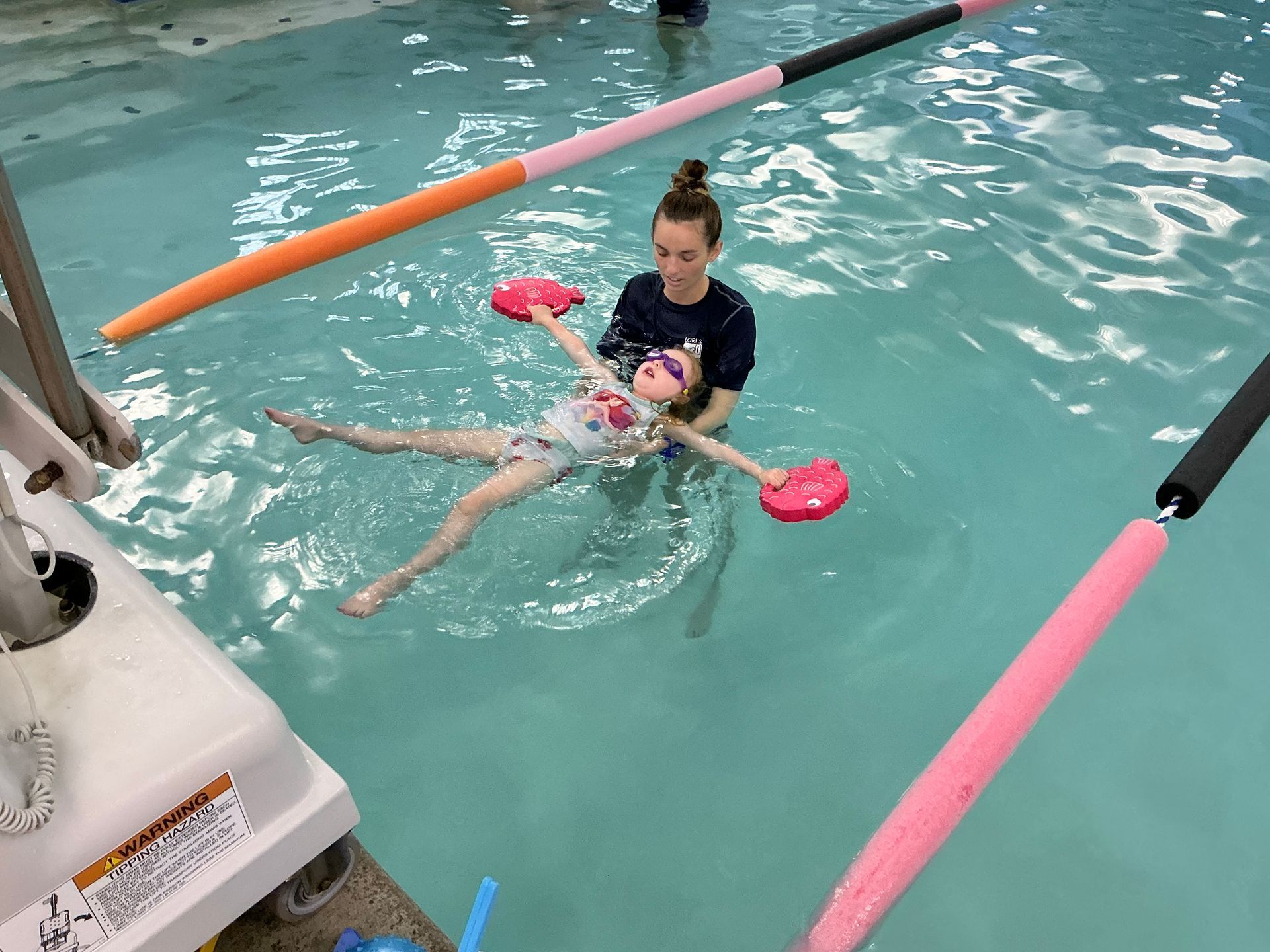 A young girl floats in a pool, supported by a woman instructor.
