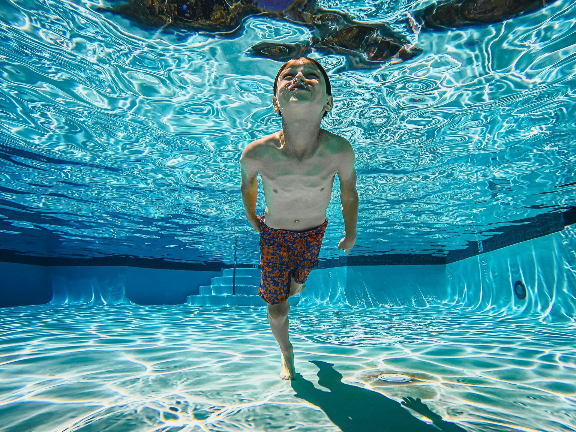 A young boy is swimming underwater in a swimming pool.