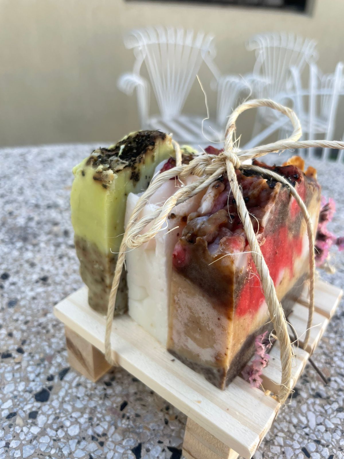 Barra de jabón colorida en capas atada con cordel sobre una pequeña paleta de madera, decorada con flores secas.