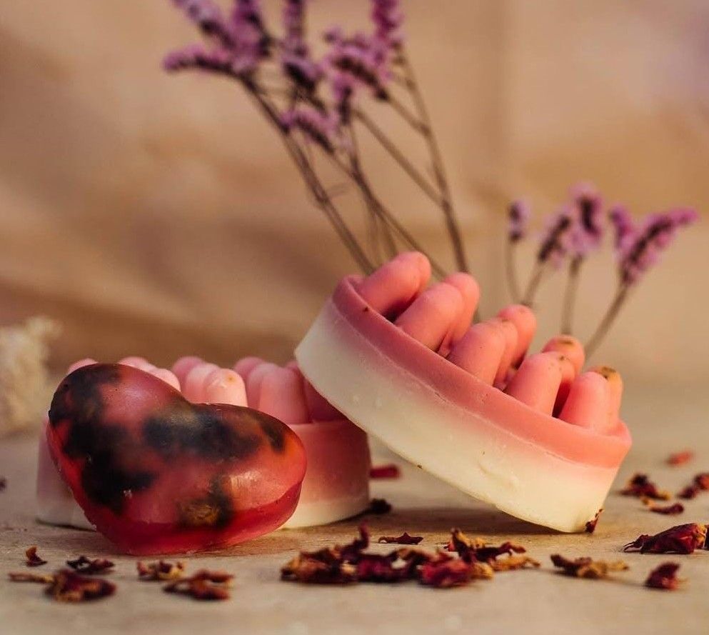 Jabones en forma de corazones y barras circulares con colores rosa y blanco y pétalos de rosa.