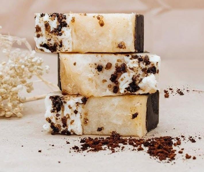 Tres jabones texturizados apilados con bases de color marrón oscuro y motas marrones sobre un fondo beige claro.