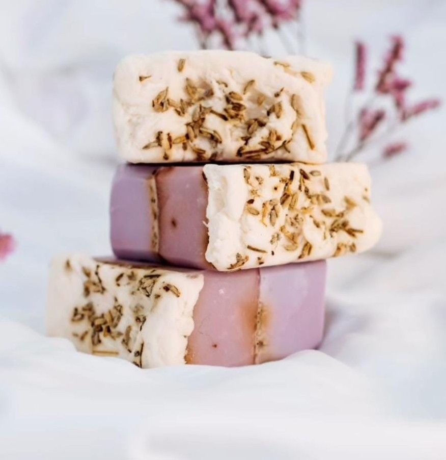 Tres barras apiladas de jabón de lavanda con hierbas secas encima, sobre un fondo blanco.