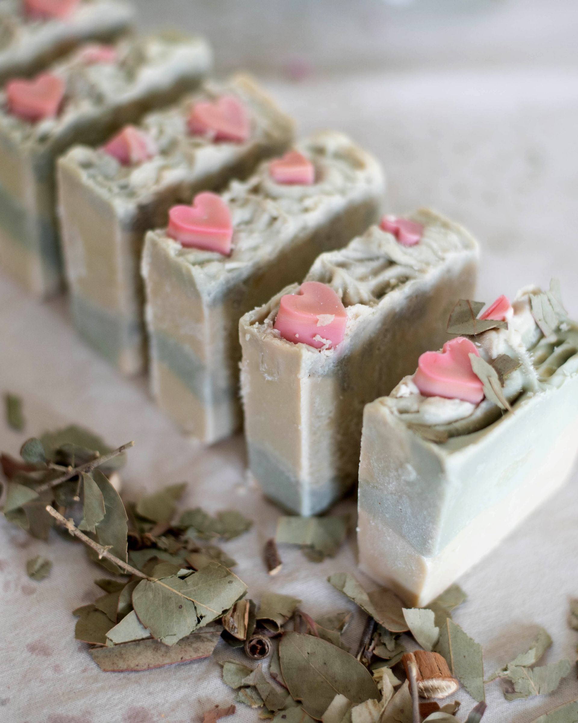 Primer plano de barras de jabón rectangulares con adornos de corazones rosas, varios tonos de verde, blanco y azul.