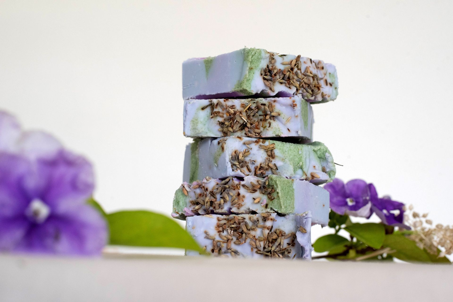 Barras de jabón artesanales, capas de lavanda y verde, acentos florales.
