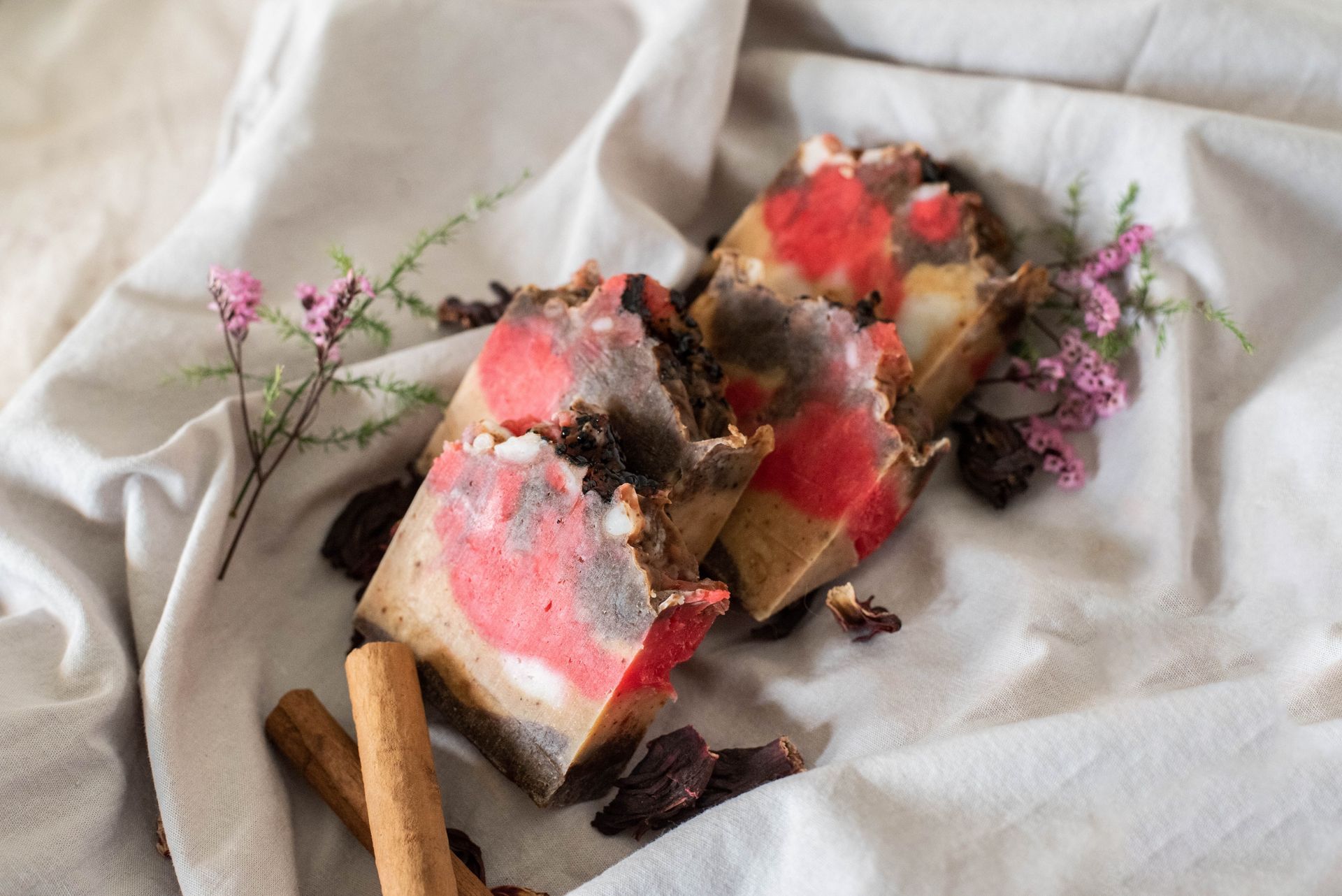 Barras de jabón apiladas con capas rojas y negras, decoradas con frutos secos, sobre una superficie blanca.
