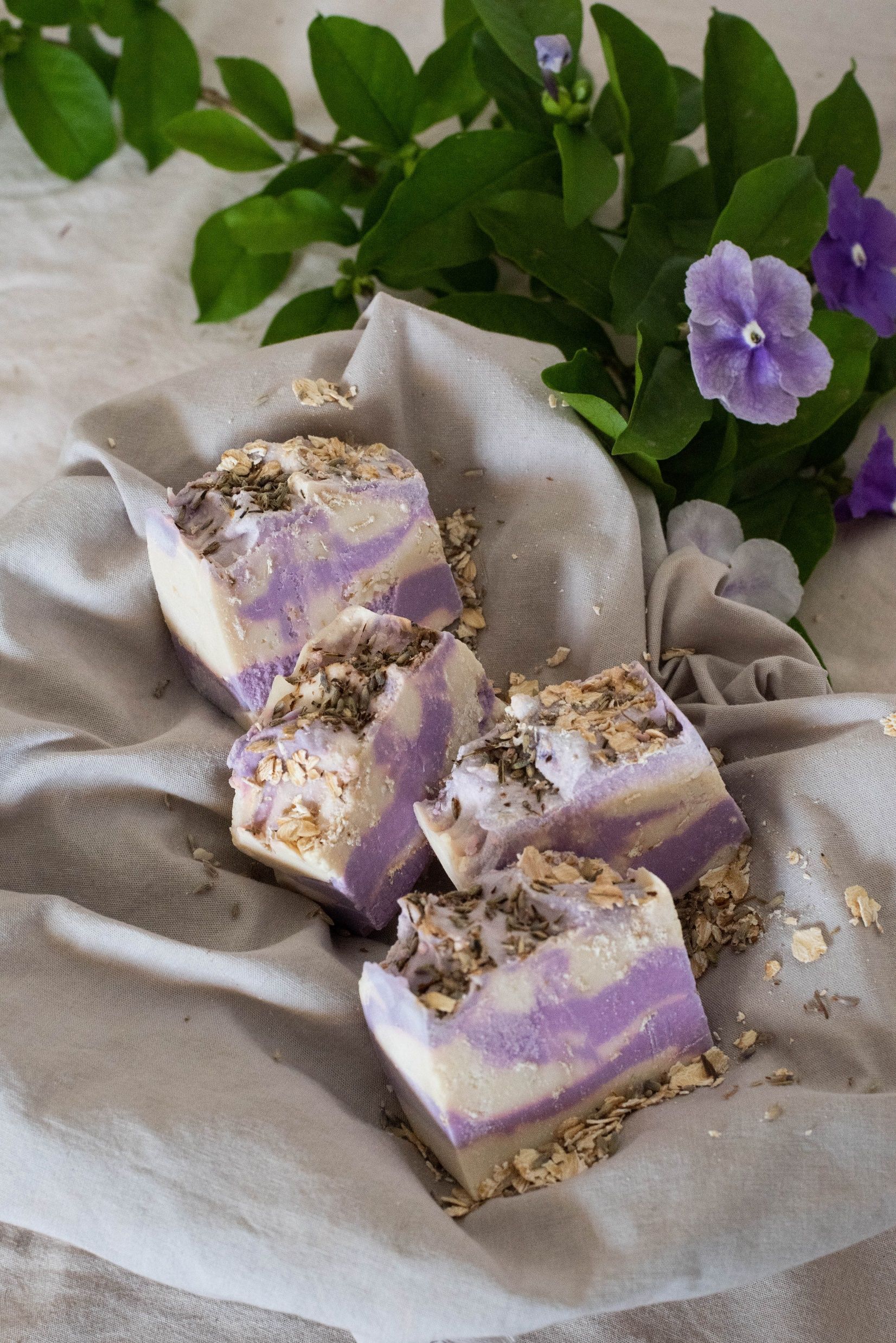Barras de jabón con remolinos de lavanda y avena, envueltas en tela y con flores.