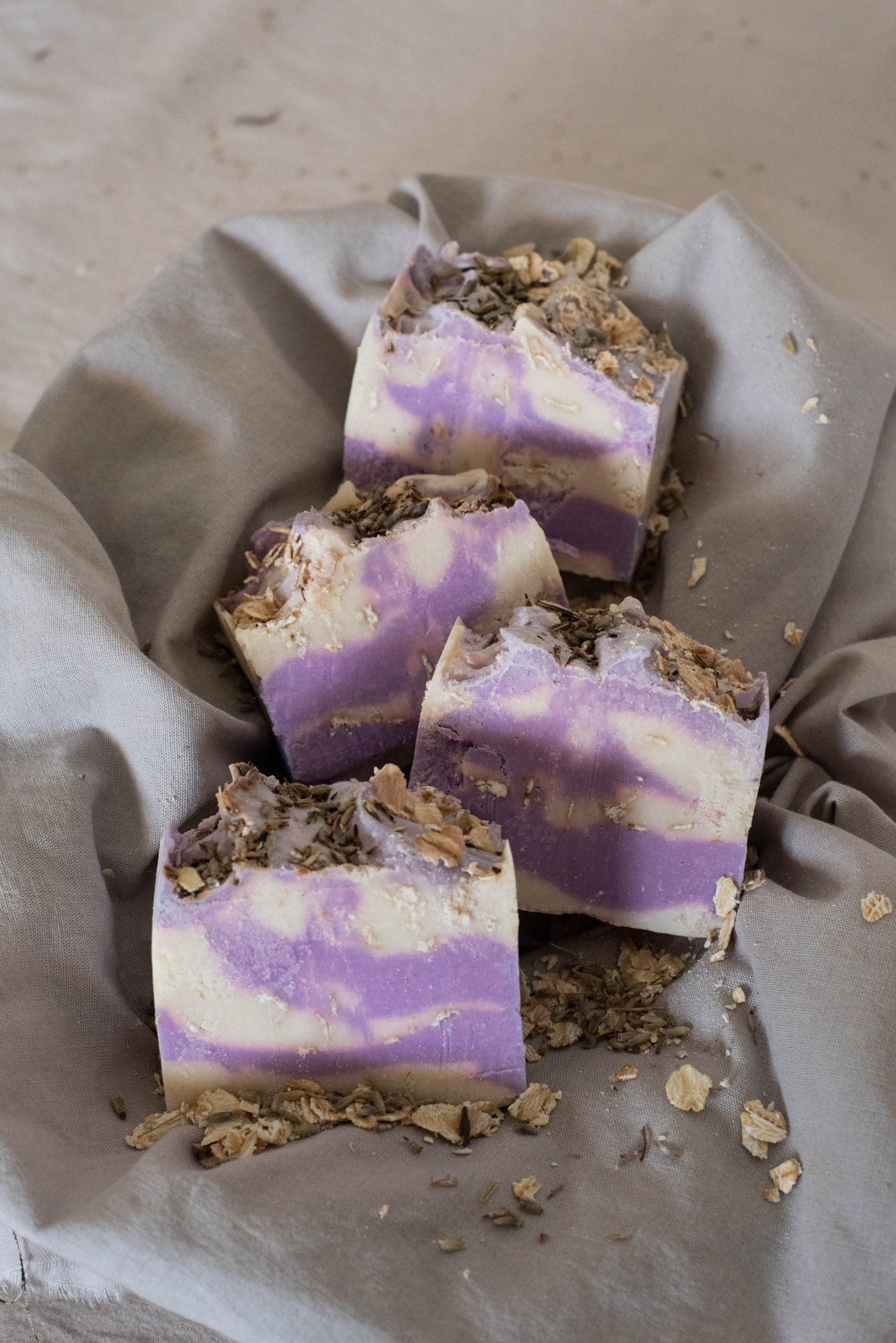 Barras de jabón con remolinos de lavanda y avena, envueltas en tela y con flores.