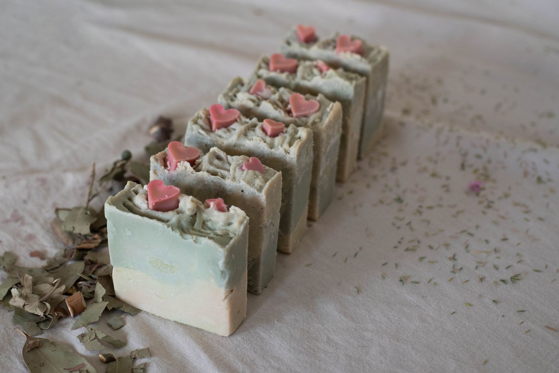 Primer plano de barras de jabón rectangulares con adornos de corazones rosas, varios tonos de verde, blanco y azul.