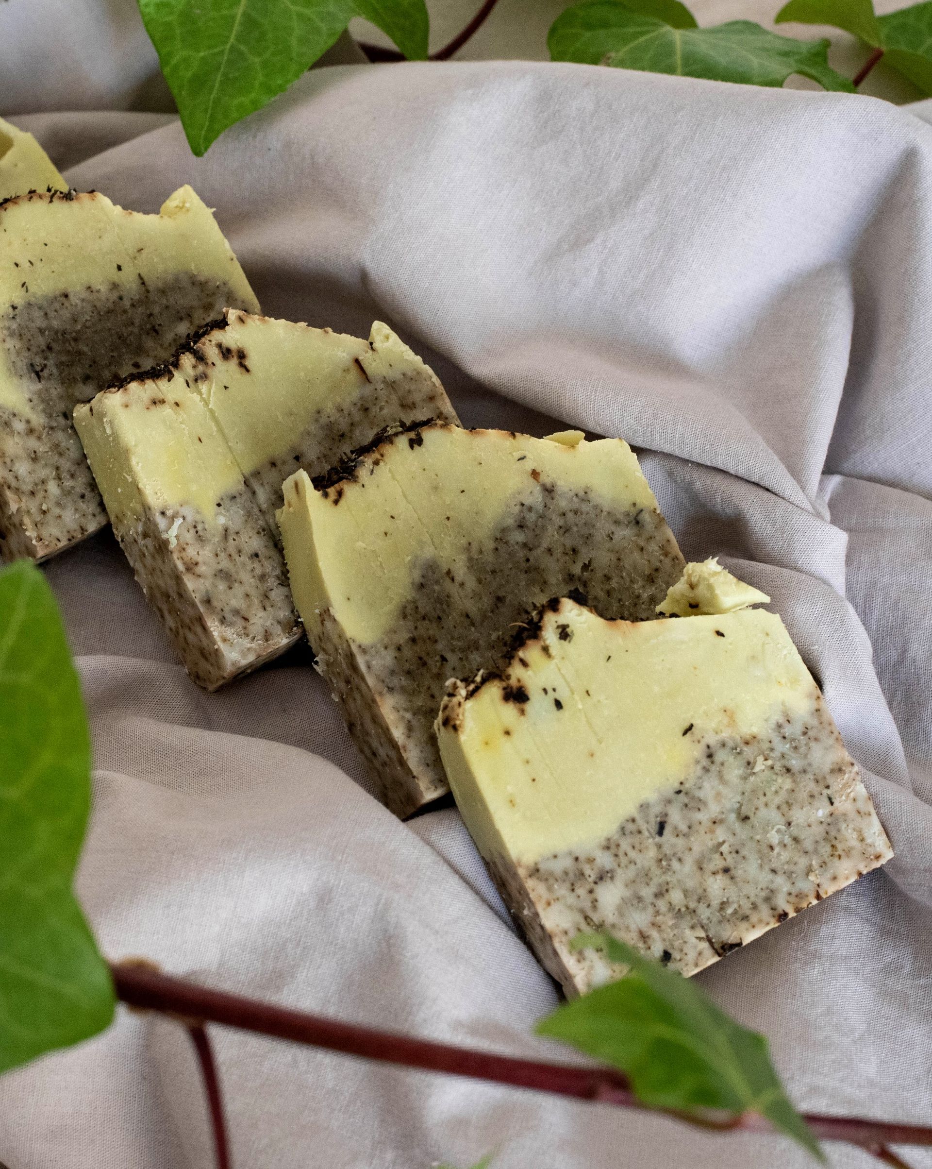 Pastillas de jabón hechas a mano, bicolor con motas, dispuestas sobre tela, rodeadas de vegetación.