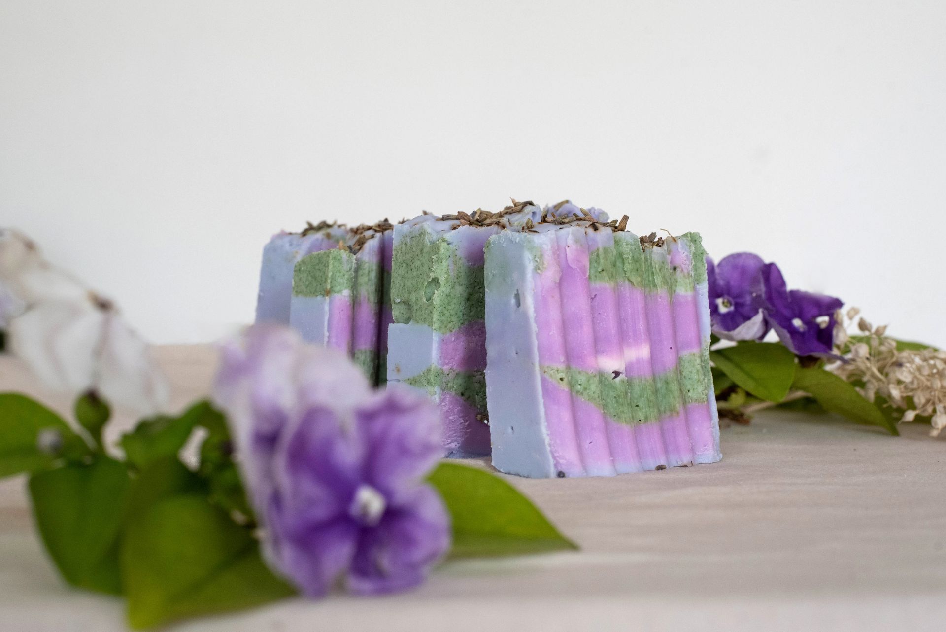 Barras de jabón artesanales, capas de lavanda y verde, acentos florales.