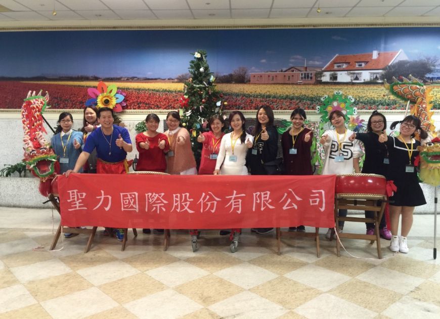 聖力國際員工團隊參與公益活動或事蹟分享,在紅色布條前豎起大拇指合影,展現企業社會責任。