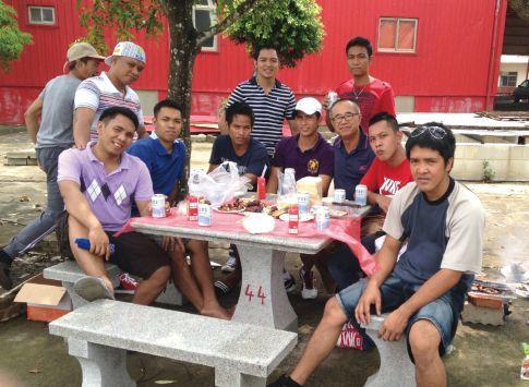 聖力國際安排的外籍移工在戶外石桌旁休閒交流與社交,背景為紅色建築與綠樹。