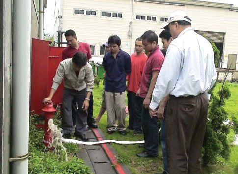 移工在戶外參加消防栓安全訓練示範,專業人員現場講解逃生安全標誌與法令宣導。