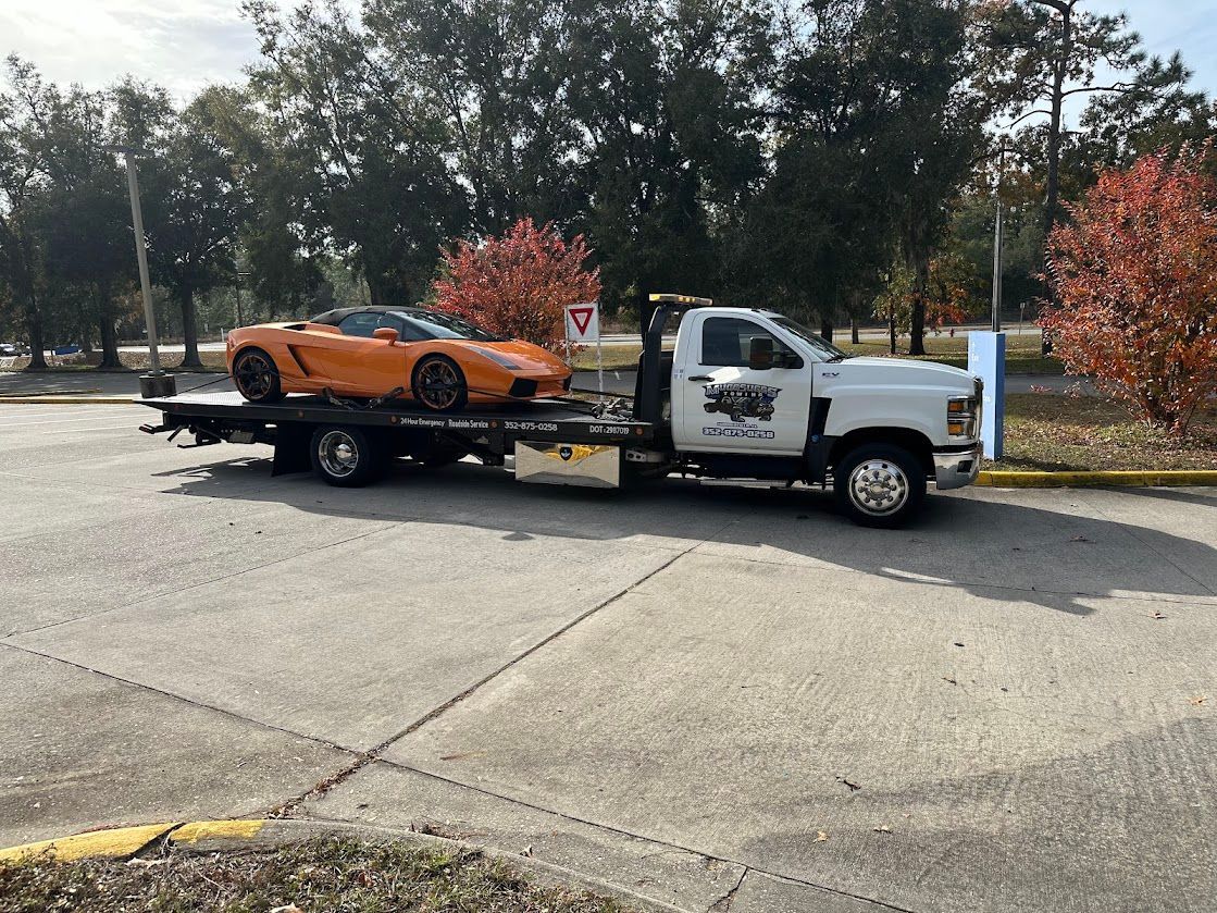 A white tow truck is towing a sports car in a parking lot.