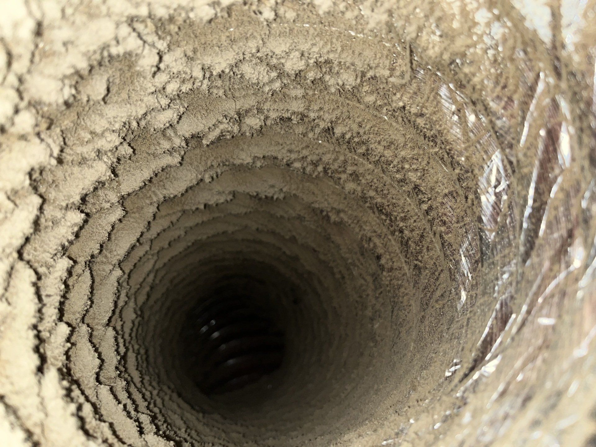 Conduit d'aération cylindrique rempli de poussière, vu de l'intérieur. Les parois sont recouvertes d'une épaisse couche de poussière et de débris.