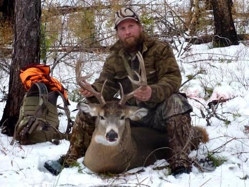 A man is kneeling down next to a deer in the snow.