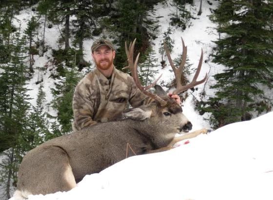 A man is holding a large deer in the snow
