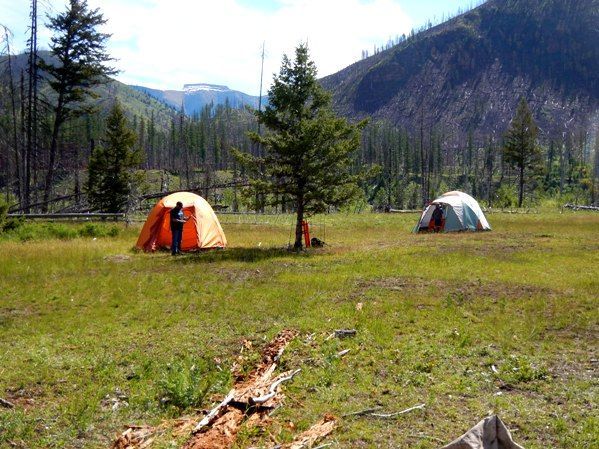 Two tents are sitting in a grassy field with mountains in the background.
