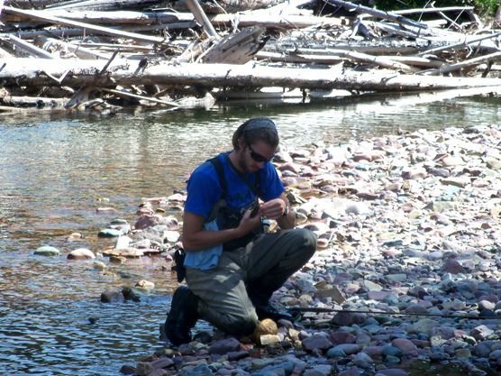 A man in a blue shirt is kneeling next to a river
