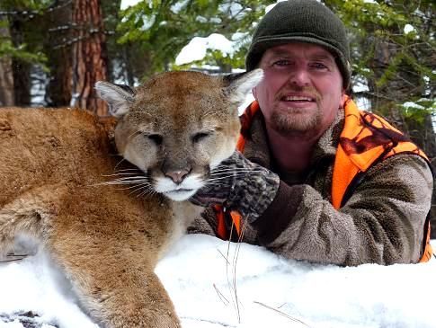 A man is posing for a picture with a mountain lion in the snow.