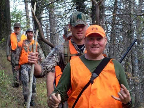 A group of hunters wearing orange vests are walking through the woods