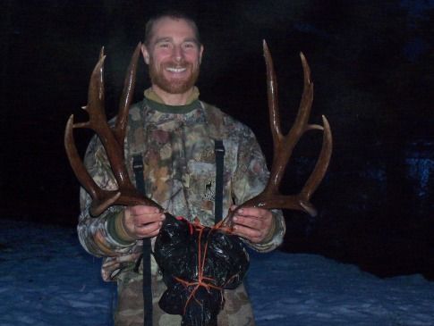 A man in a camouflage shirt is holding a large deer antlers
